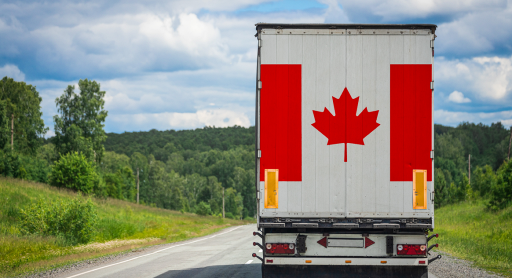 A delivery truck with the Canadian flag on the back drives down a road, surrounded by green trees.